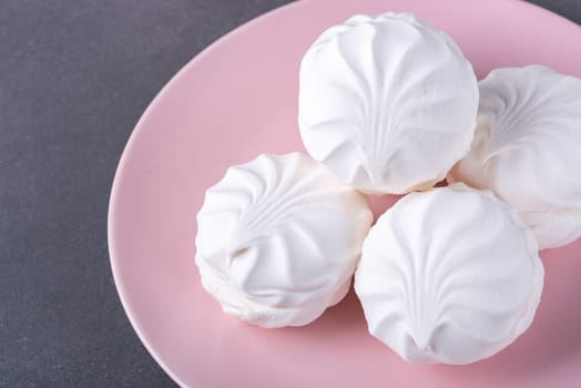 White fluffy marshmallows or marshmallow shells with powdered sugar sprinkles on a pink plate on a grey table.