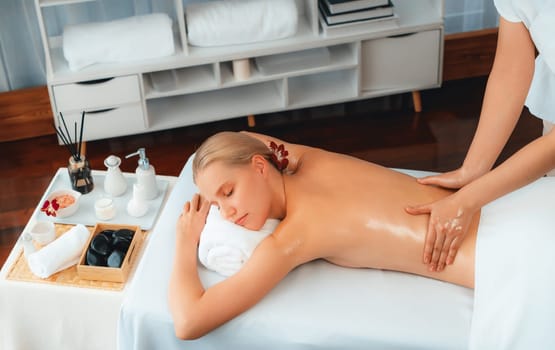 Caucasian woman customer enjoying relaxing anti-stress spa massage and pampering with beauty skin recreation leisure in day light ambient salon spa at luxury resort or hotel. Quiescent