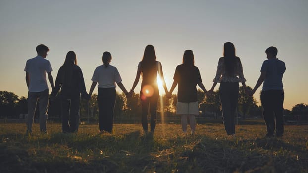 Friends standing holding hands at sunset