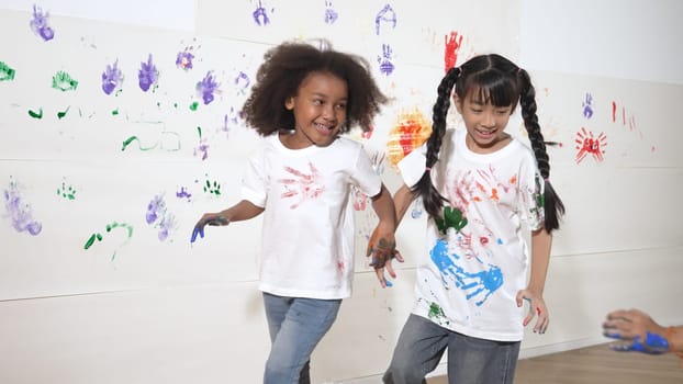 Playful children playing and running with colorful stained hand in front of white background. Funny happy multicultural students enjoy attending in art lesson. Creative activity concept. Erudition.