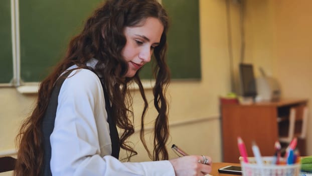 Schoolgirl as a teacher sits at a desk and writes something