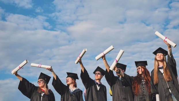 Cheerful graduates pose with raised diplomas on a sunny day