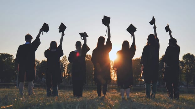 Silhouettes of college graduates waving their caps at sunset