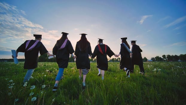 Six graduates in robes walk against the backdrop of the sunset