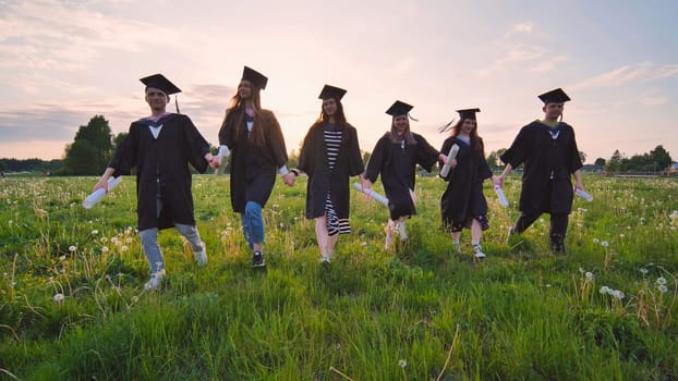 Six graduates in robes walk against the backdrop of the sunset
