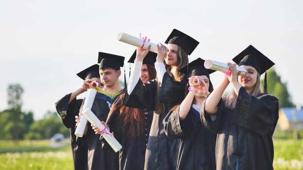 Cheerful graduates on a sunny day look through diplomas like a telescope