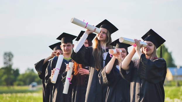 Cheerful graduates on a sunny day look through diplomas like a telescope