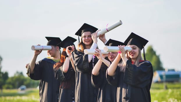 Cheerful graduates on a sunny day look through diplomas like a telescope