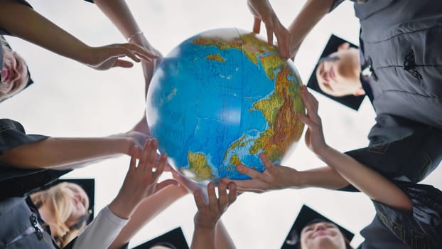 Graduating students twirl a geographic globe of the world in their hands