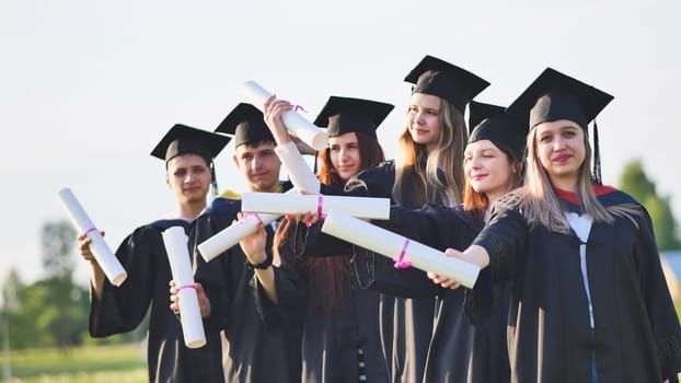 Cheerful graduates pose with raised diplomas on a sunny day