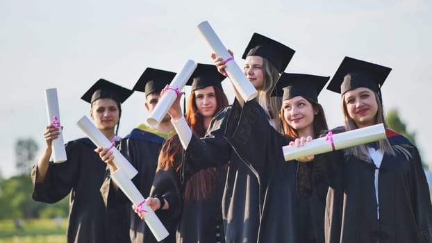 Cheerful graduates pose with raised diplomas on a sunny day