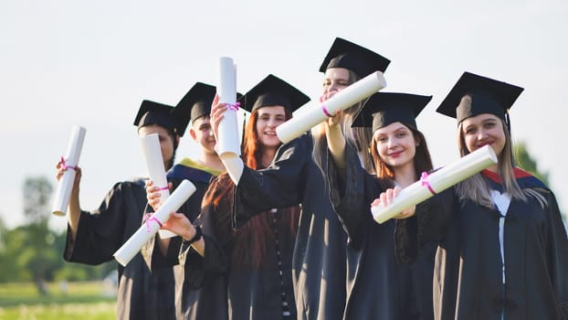 Cheerful graduates pose with raised diplomas on a sunny day