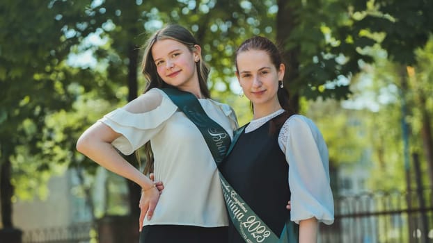 Two Russian schoolgirls graduate posing on a summer day