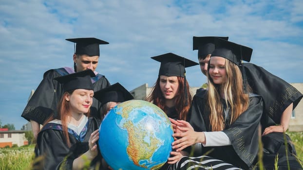 Graduates in black robes examine a geographical globe sitting on the grass