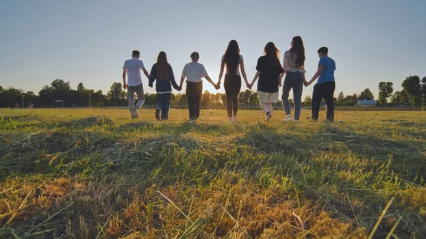 Friends at sunset holding hands walking towards the sun