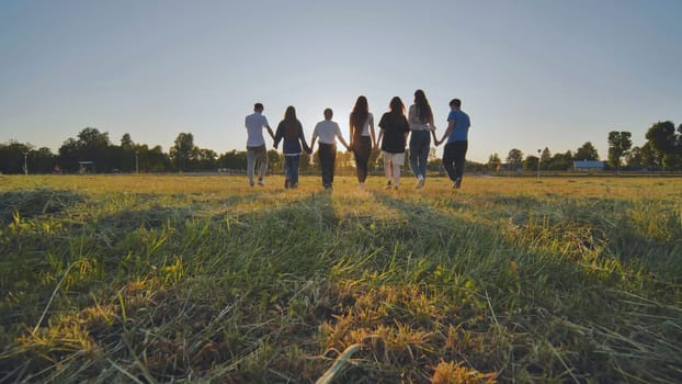 Friends at sunset holding hands walking towards the sun