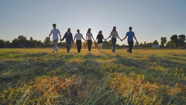 Friends at sunset holding hands walking towards the sun