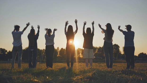 Young friends stand at sunset and wave their hands at the sun