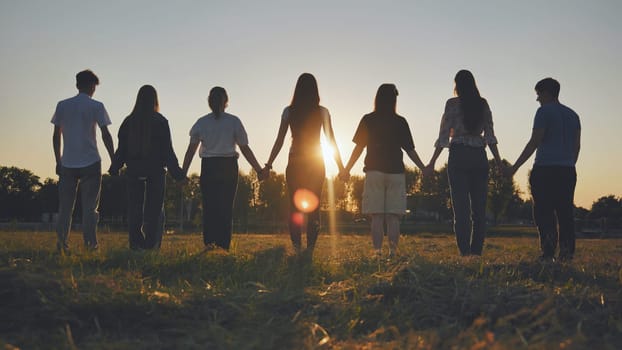 Friends standing holding hands at sunset