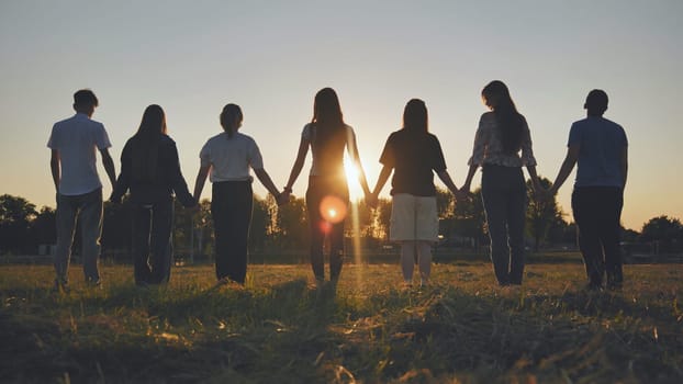 Friends standing holding hands at sunset