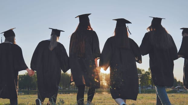 College graduates hold hands at sunset to meet the future and the sun