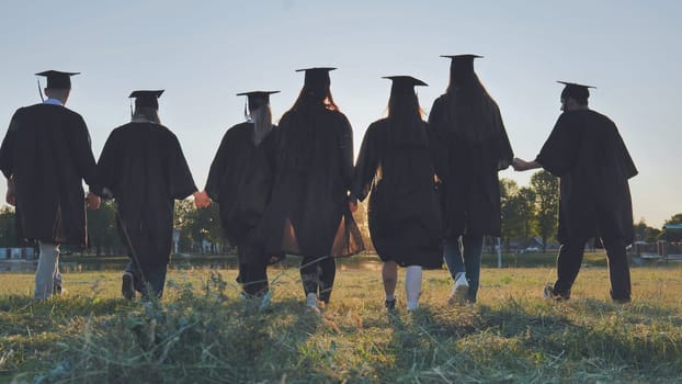 College graduates walk at sunset holding hands