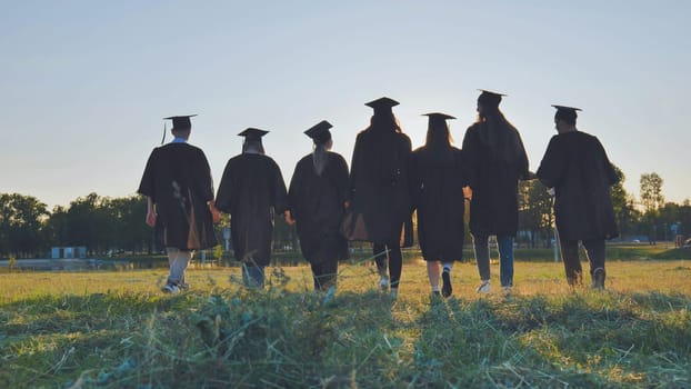 College graduates walk at sunset holding hands