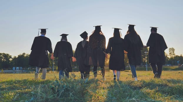 College graduates hold hands at sunset to meet the future and the sun