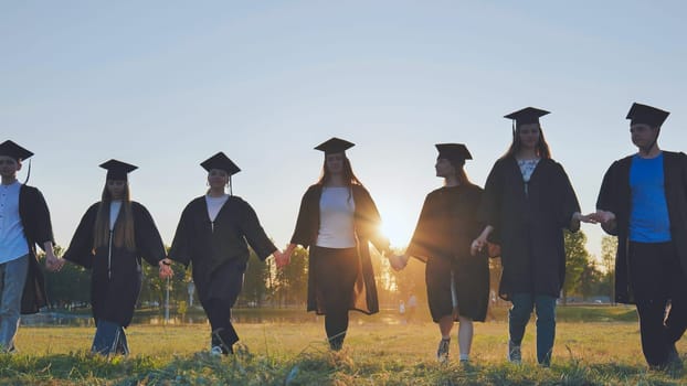 College graduates walk at sunset holding hands