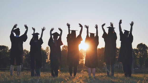 College graduates in robes waving at sunset