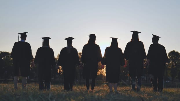 Silhouettes of college graduates standing in a meadow