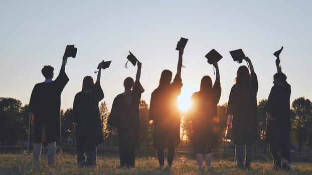 Silhouettes of college graduates waving their caps at sunset