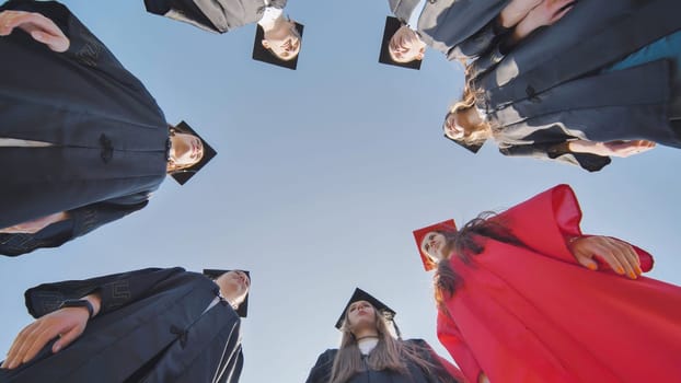 Graduates in robes stand in a circle. View from below