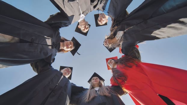 College graduates in a circle stand hugging each other