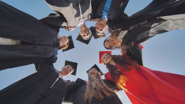 College graduates in a circle stand hugging each other