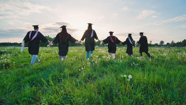 Six graduates in robes walk against the backdrop of the sunset