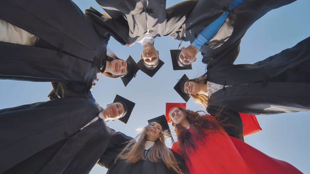 College graduates in a circle stand hugging each other