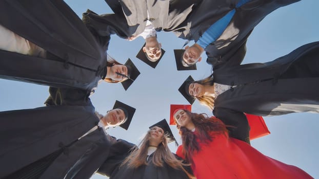 College graduates in a circle stand hugging each other