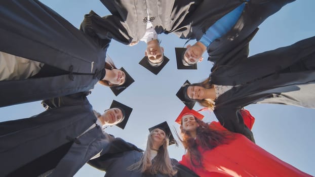 College graduates in a circle stand hugging each other