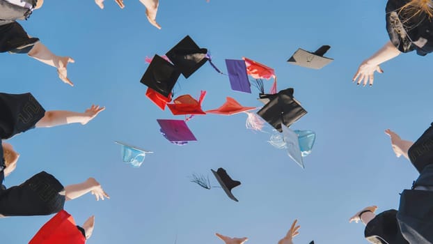 Graduates tossing multicolored hats against a blue sky