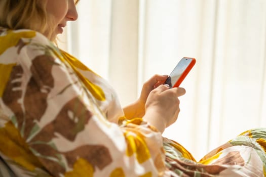 Happy millennial girl checking social media holding a smartphone sitting on the sofa.