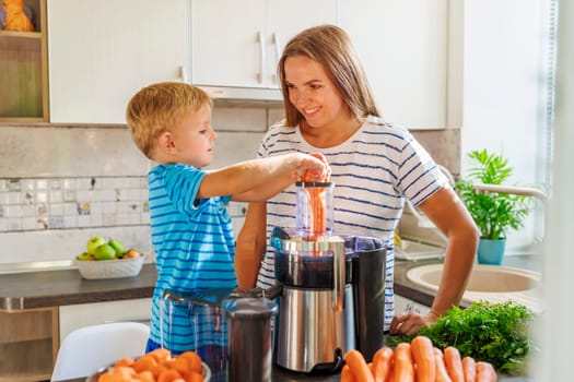 A young boy learns how to make carrot juice under his mother's guidance in a sunny home kitchen, surrounded by fresh ingredients.