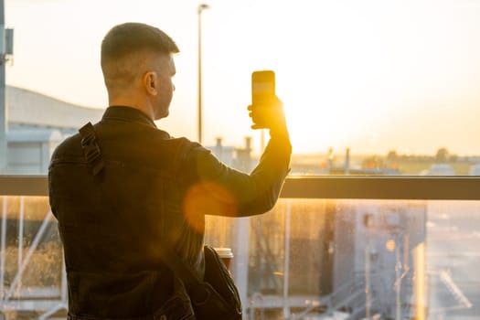 A young man takes photo standing in the airport at sunset.