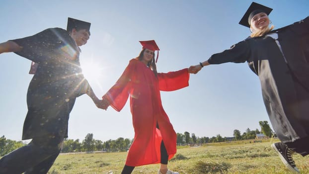 College graduates holding hands run in a round dance