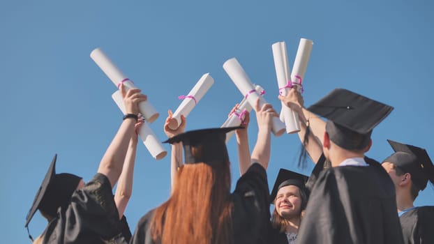 College graduates with caps tie their diplomas together