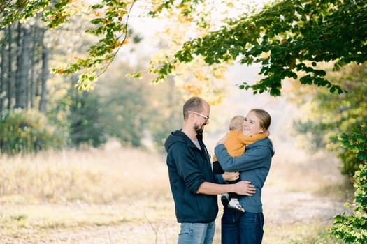 Dad hugs mom with a little boy in her arms on a green lawn. High quality photo