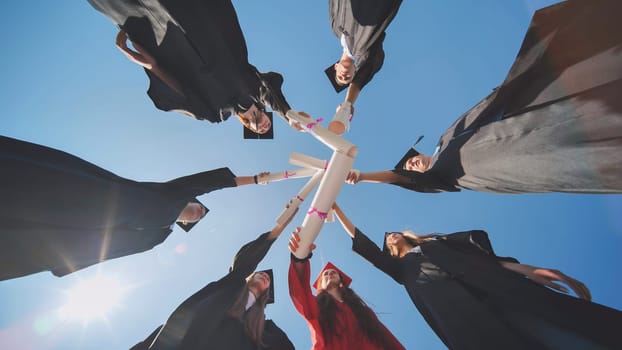 College graduates join hands with diplomas standing in a circle