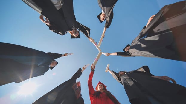 College graduates join hands with diplomas standing in a circle