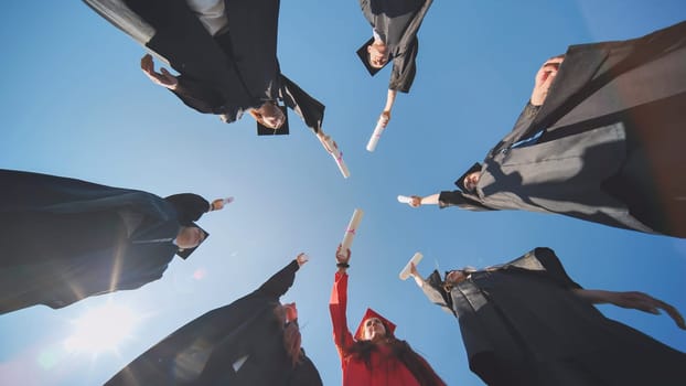 College graduates join hands with diplomas standing in a circle