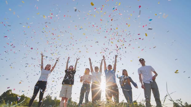 Friends toss colorful paper confetti from their hands against the rays of the evening sun